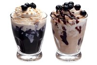Two layered dessert drinks with whipped cream and berries in clear glasses isolated on white background for cafe menu design.