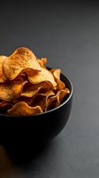 Crispy golden potato chips in black bowl on dark background, crunchy snack food for appetizer and party concepts.