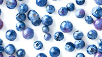 Fresh ripe blueberries scattered on white background with purple highlights and natural texture, organic farm produce pattern for healthy eating concept.