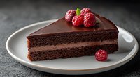 Slice of dark chocolate layer cake with chocolate ganache frosting and fresh raspberries on white plate against dark background. Food photography.