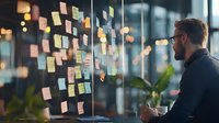 Caucasian businessman analyzing sticky notes on glass wall during strategic planning session, holding coffee in modern office with bokeh lights.