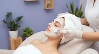 Professional cosmetologist applying facial mask treatment to relaxed woman client in modern spa salon with plants and purple wall background.
