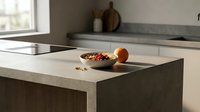 Minimalist kitchen island with concrete countertop, wooden bowl of colorful cereal, fresh orange fruit, and tablet device for cooking recipes and meal planning.
