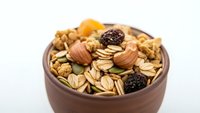 Healthy mixed nuts and dried fruits in wooden bowl on white background. Nutritious snack mix with almonds, walnuts and raisins for organic food concepts.