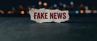 Torn paper with fake news text against blurred city lights background representing misinformation and media literacy concepts for editorial use.