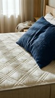 Cozy bedroom interior with navy blue pillows on quilted beige bedding, wooden headboard, soft window curtains, and warm natural light for home decor and lifestyle design projects.