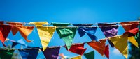 Colorful bunting flags strung across bright blue sky, featuring red, yellow, green, blue, and purple triangular pennants for festive celebrations and outdoor party decorations.