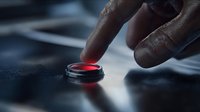 Close-up of male finger pressing glowing red button on dark control panel, dramatic lighting creating tense atmosphere for emergency or security concepts.