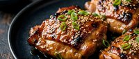 Glazed chicken thighs with sesame seeds and herbs in cast iron skillet. Crispy skin poultry dish garnished with green onions for culinary presentations.
