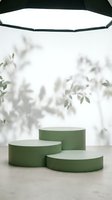 Green cylindrical podiums on marble surface with soft natural lighting and blurred foliage background for product display and presentation.