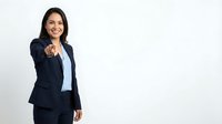 Professional Hispanic businesswoman in dark suit pointing forward with confident smile on white background for corporate presentations.