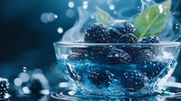 Fresh blackberries in clear glass bowl with water splash and droplets creating dynamic composition against dark blue background with bokeh effect.