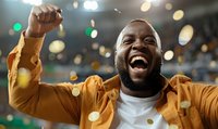 Young African American man celebrating victory with raised fist, wearing yellow jacket and white t-shirt, expressing pure joy and excitement against blurred bokeh lights background.