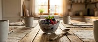 Healthy breakfast bowl with granola, fresh berries, and yogurt on rustic wooden table in bright kitchen with natural sunlight for food blogging and wellness content.