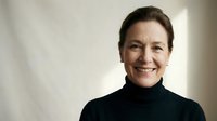 Professional mature Caucasian businesswoman in black turtleneck smiling confidently in modern office setting for corporate marketing materials.