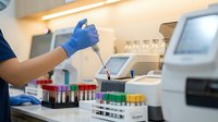 Laboratory technician in blue gloves using pipette for sample analysis with test tubes and modern equipment in medical research facility.