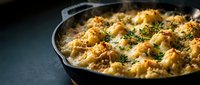 Golden baked cauliflower gratin with herbs in cast iron skillet, comfort food casserole dish for family dinner and holiday meals.