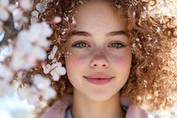 Young mixed race woman with curly hair and freckles smiling among spring cherry blossoms, natural beauty portrait in soft sunlight with bokeh effect.