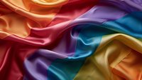 Luxurious rainbow colored silk fabric with soft folds and waves creating elegant drapery texture. Smooth satin material in vibrant spectrum of colors flows gracefully.
