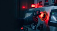 Industrial worker operating heavy machinery with glowing red emergency stop button in dark manufacturing facility for safety training materials.