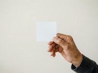 Hand holding blank white square card against neutral beige background, suitable for mockups, branding, and promotional material presentations.