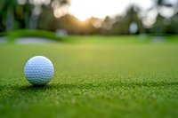 White golf ball on green grass course at sunset with soft bokeh background and copy space, close up view for sports and recreation design.