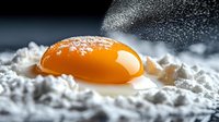 Fresh raw egg yolk on white flour with falling powder, dramatic dark background with soft focus. Macro food photography for culinary concepts.