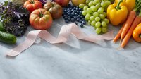 Fresh organic fruits and vegetables with pink measuring tape on marble surface promoting healthy diet and weight loss lifestyle.