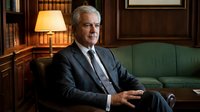 Senior Caucasian businessman in elegant suit sitting confidently in luxurious office library with warm lighting and classic wooden interior design.