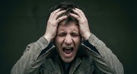 Stressed young Caucasian man screaming with hands on head showing intense frustration and mental breakdown against dark background for stress concepts.