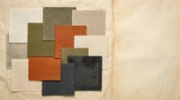 Fabric swatches in earth tones arranged on wooden surface showing textile samples in orange, green, beige and gray colors for interior design projects.