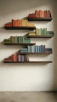 Colorful books arranged on floating wooden shelves against white brick wall creating modern library display for home office or study room interior design.