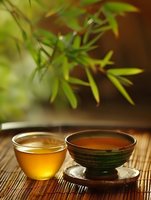 Traditional tea ceremony with glass cup and ceramic bowl on bamboo mat, fresh green leaves creating serene atmosphere for wellness and relaxation.