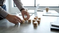 Businessman arranging wooden blocks with arrows on office desk, symbolizing strategy, direction, and decision-making in business planning.