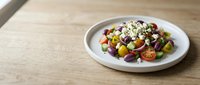 Colorful salad with mixed vegetables, beans, corn, and crumbled cheese on white plate over wooden table surface for food photography and culinary content.