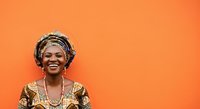 Mature African woman wearing traditional gold patterned clothing and headwrap smiling against vibrant orange background for portrait and cultural representation projects.