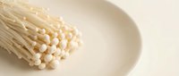 Bunch of white enoki mushrooms on a ceramic plate, isolated on neutral background for culinary and food styling projects.