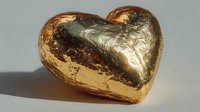 Golden heart-shaped chocolate candy with metallic foil wrapper on neutral background for Valentine's Day, romance, love celebration and sweet treats.