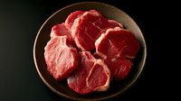 Fresh raw beef ribeye steaks arranged on dark ceramic plate against black background, dramatic lighting highlights meat texture and marbling for culinary use.