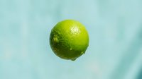 Fresh green lime with water droplets isolated on light blue background, suitable for food and beverage marketing, healthy eating campaigns, and culinary design projects.