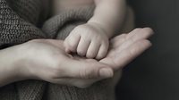 Tender moment of parent holding baby hand showing love, care and protection in family bonding scene with soft natural lighting and warm atmosphere.