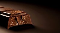 Dark chocolate bar with water droplets on rich brown surface creating luxurious confectionery mood for gourmet dessert and culinary photography.
