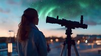Young woman with long hair observing northern lights through telescope against night sky with aurora borealis and city lights in background, winter stargazing moment.