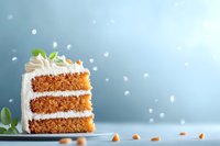 Slice of layered carrot cake with cream cheese frosting, decorated with mint leaves and nuts on blue background, soft bokeh effect and copy space.