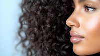 Young African American woman with natural curly dark hair and glowing skin in profile view against blue background, showcasing natural beauty and healthy hair texture.