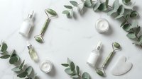 Natural skincare cosmetics with eucalyptus leaves and jade rollers arranged on white marble background for spa and beauty wellness routine.