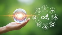 Hand holding glowing sphere with CO2 carbon footprint reduction icons on green background for environmental sustainability and climate action.