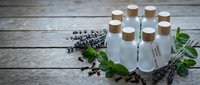 Essential oil bottles with cork stoppers surrounded by fresh lavender and mint herbs on rustic wooden background for aromatherapy and natural wellness.