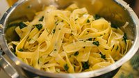 Fresh fettuccine pasta with herbs in stainless steel pan, close up view of traditional Italian cuisine prepared with parsley garnish.