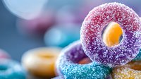 Colorful sugar coated gummy candy rings in vibrant purple, blue and yellow colors stacked together with sparkling crystalline texture on blurred background.